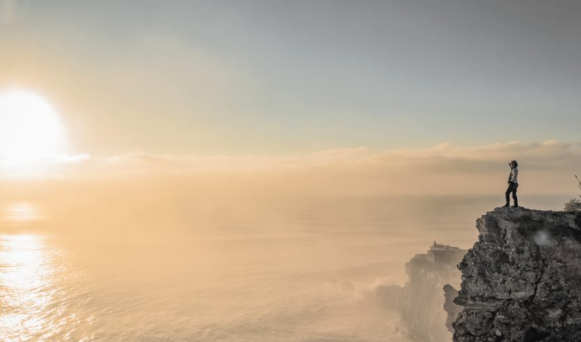 Osoba stoji na litici iznad mora i promatra horizont kao simbol promjene perspektive, osobnog rasta i razvoja svijesti.