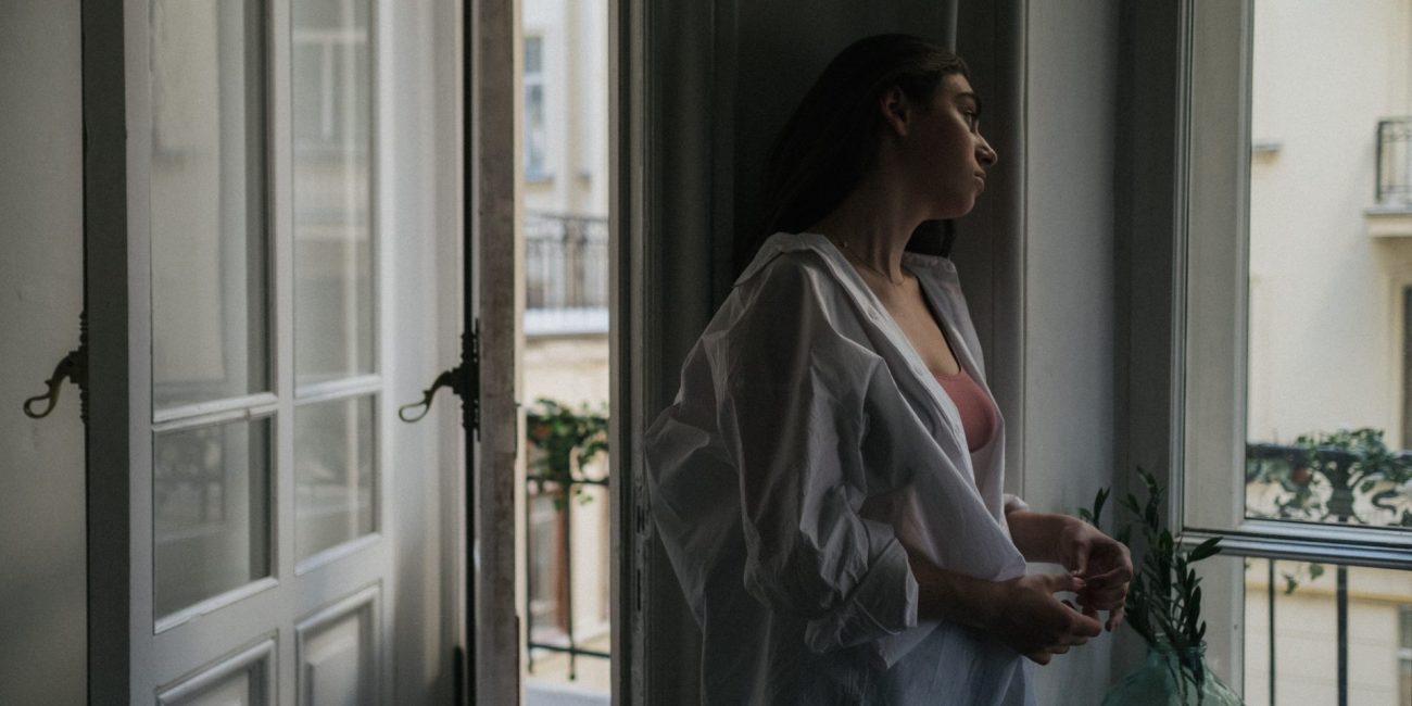 Žena stoji uz otvoren prozor tijekom toplinskog vala pokušavajući pronaći osvježenje u vrućem ljetnom danu