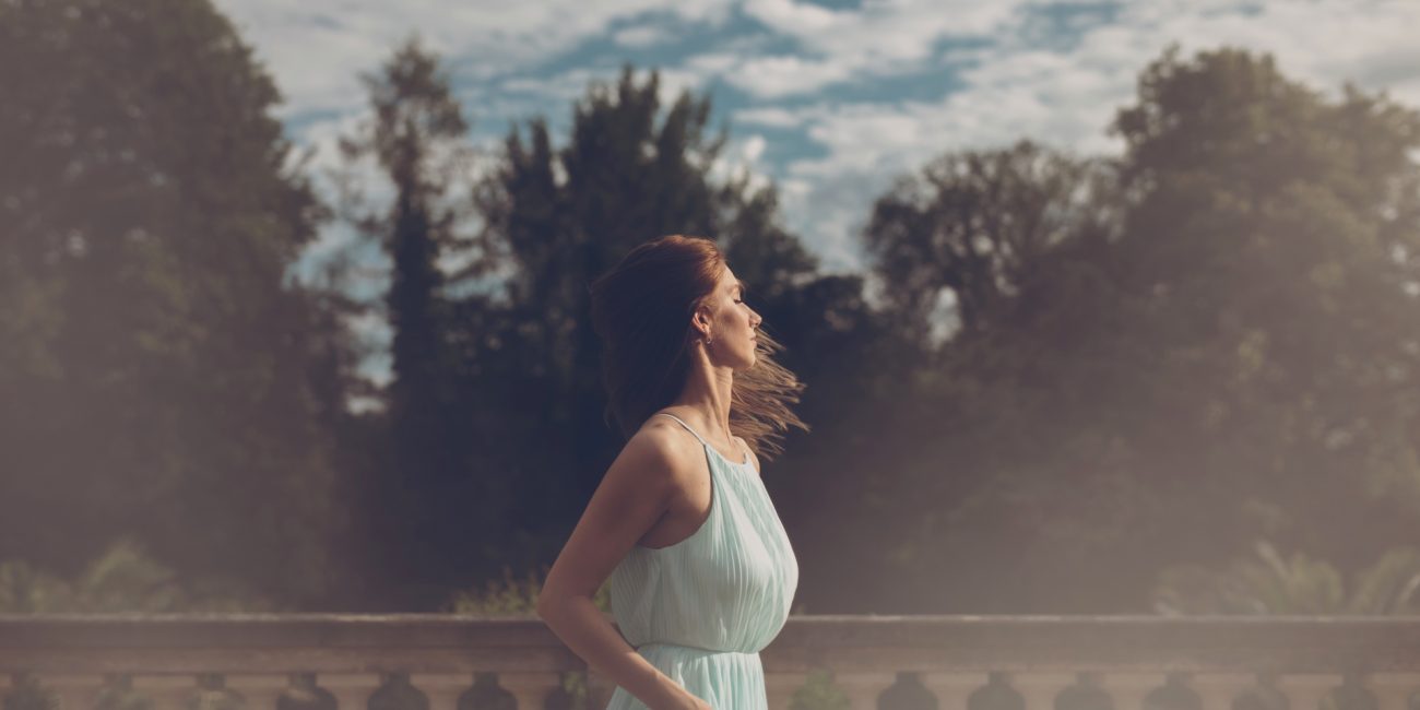 Žena u haljini stoji na elegantnoj terasi okrenuta prema svjetlu, simbolizirajući skl