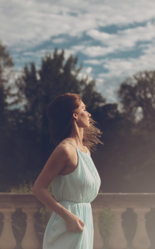 Žena u haljini stoji na elegantnoj terasi okrenuta prema svjetlu, simbolizirajući skl